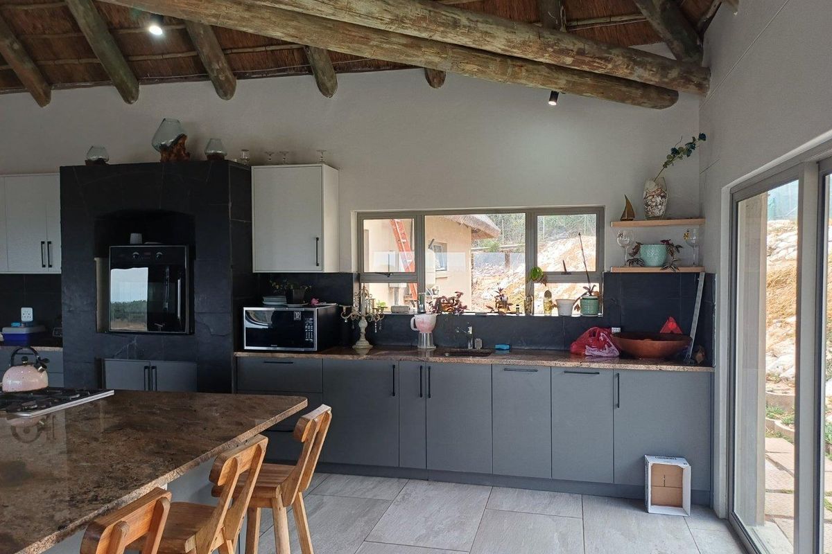 Modern kitchen featuring dark cabinetry, stone countertops, a built-in oven, and a unique exposed timber beam thatched ceiling.