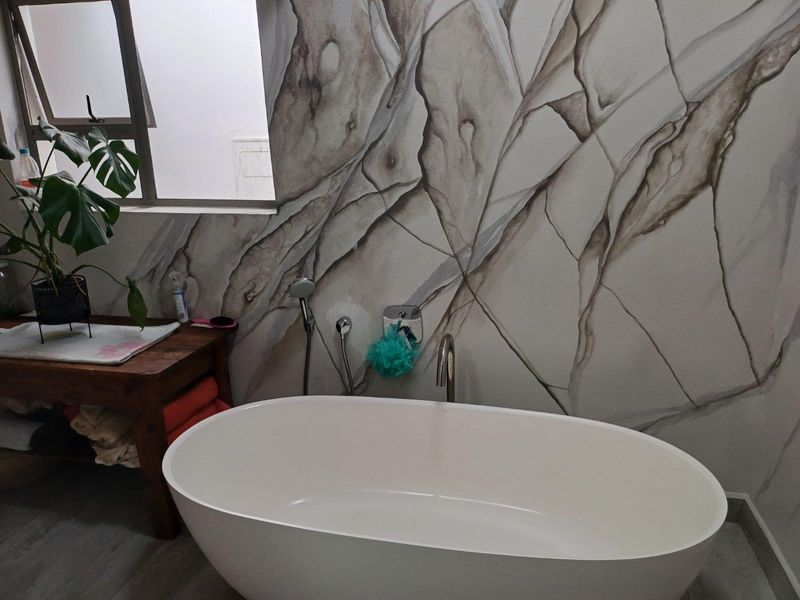 A modern bathroom featuring a freestanding white bathtub set against a decorative stone-effect feature wall with integrated plumbing fixtures.