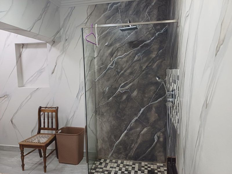 A bathroom featuring a walk-in shower with a glass screen, dark marble-effect wall cladding, and a mosaic tiled shower floor.