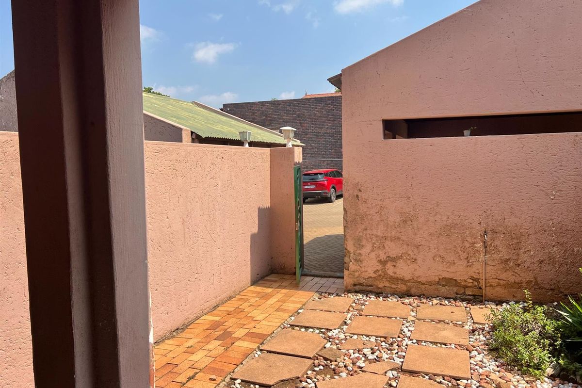 A view of the exterior rear courtyard featuring paved walkways, stone accents, and access to the driveway area.