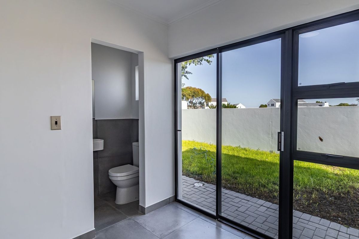 A bright living area featuring large sliding glass doors that open onto a paved patio and garden, with an adjacent compact bathroom.
