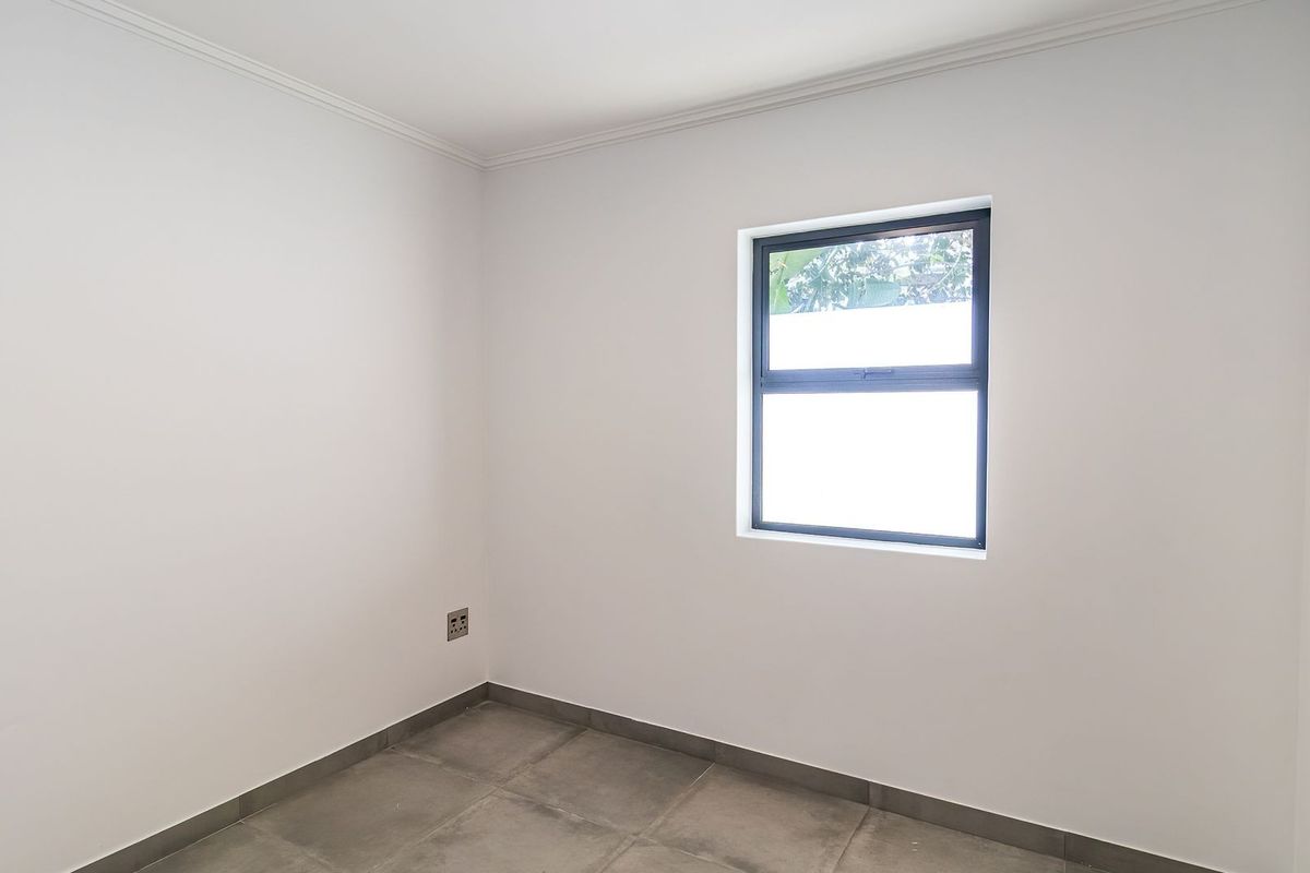 A clean, empty bedroom featuring neutral white walls, grey tiled flooring, and a modern window with dark framing.