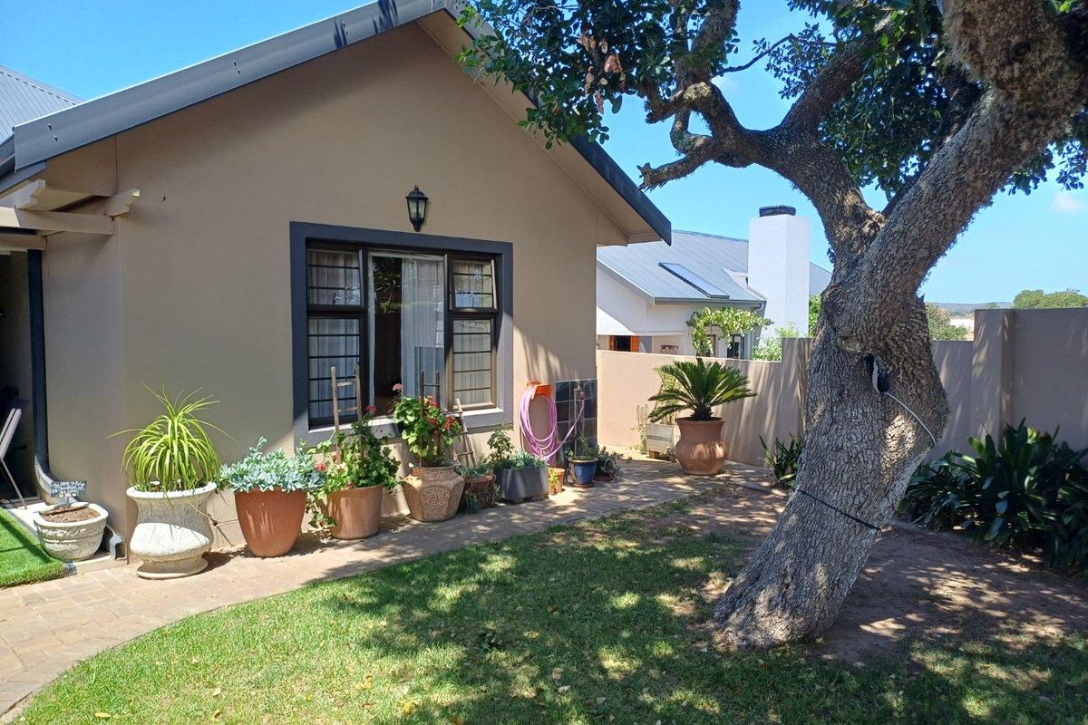 A view of the rear exterior of the house, featuring a paved walkway, landscaped garden area, and mature tree.