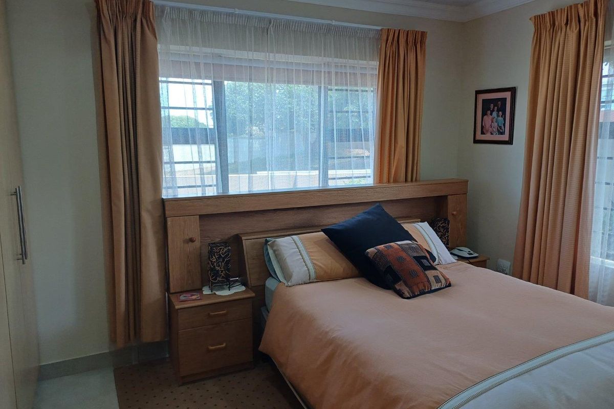 A bedroom featuring a built-in wooden headboard with integrated bedside tables and large windows with curtains.