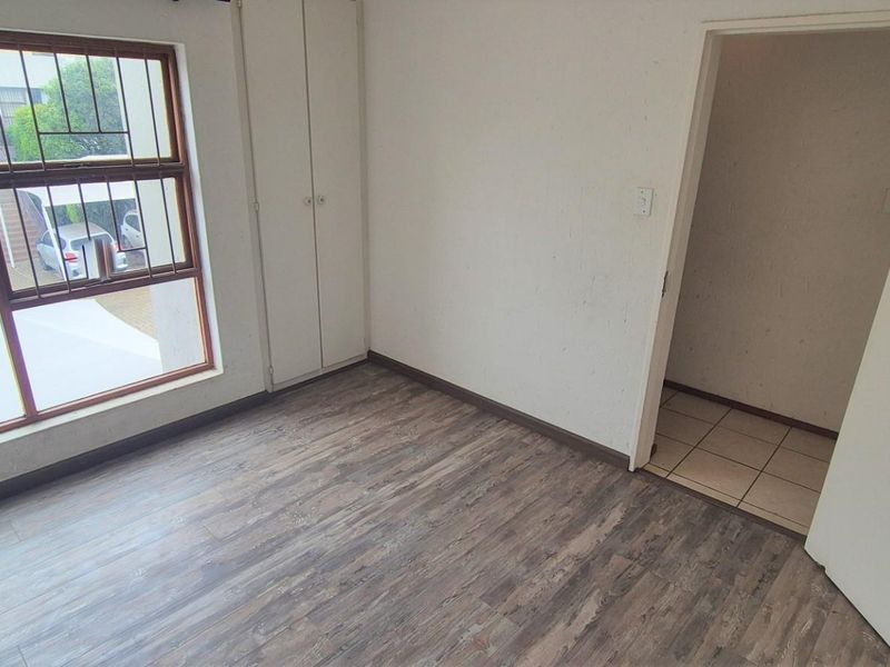 An empty bedroom featuring laminate flooring, built-in cupboards, and a window with security bars, offering a blank canvas for personalization.