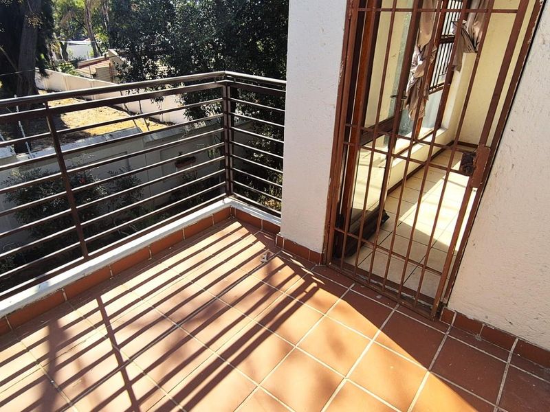 A private balcony featuring tiled flooring and a metal security gate, overlooking the surrounding greenery.