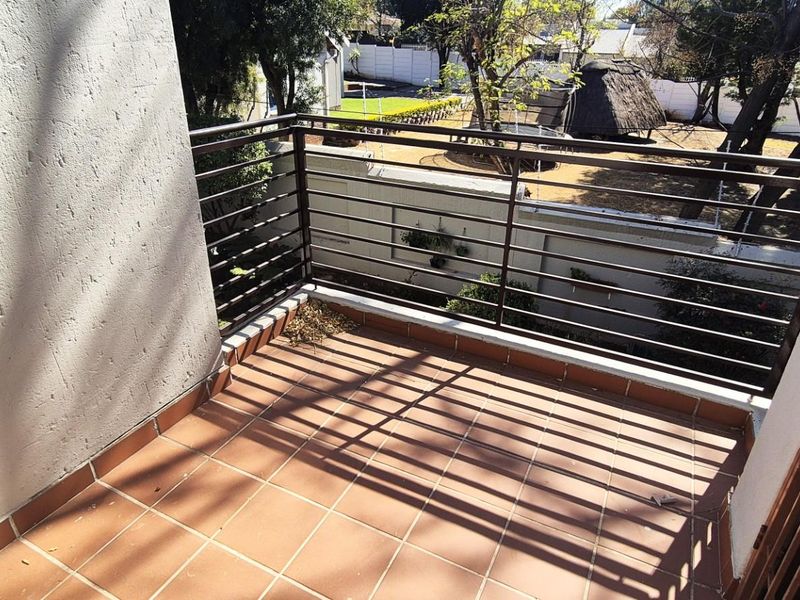 A private balcony featuring tiled flooring and a metal balustrade, offering an elevated view of the surrounding garden area.