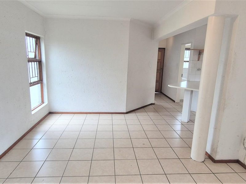 An empty open-plan living area featuring ceramic floor tiles, a structural column, and a breakfast counter leading into the kitchen space.