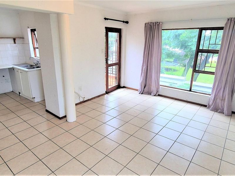 Open-plan living area featuring tiled floors, a functional kitchen with built-in appliances, and direct access to the exterior through a security door.