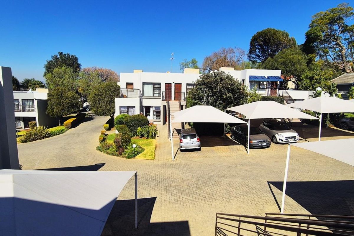 An elevated view of the apartment complex grounds featuring paved driveways, covered parking bays, and established garden areas.