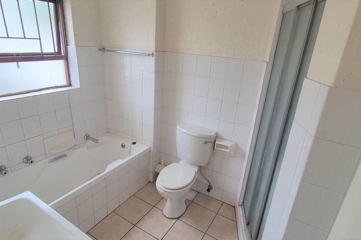 A dated bathroom featuring a built-in bathtub, toilet, and separate shower enclosure with white wall tiling and floor tiles.