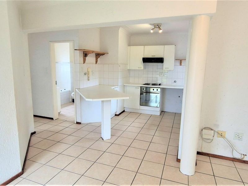 Open-plan kitchen area featuring built-in cabinetry, oven, hob, extractor fan, and a breakfast counter, finished with neutral tiled flooring.