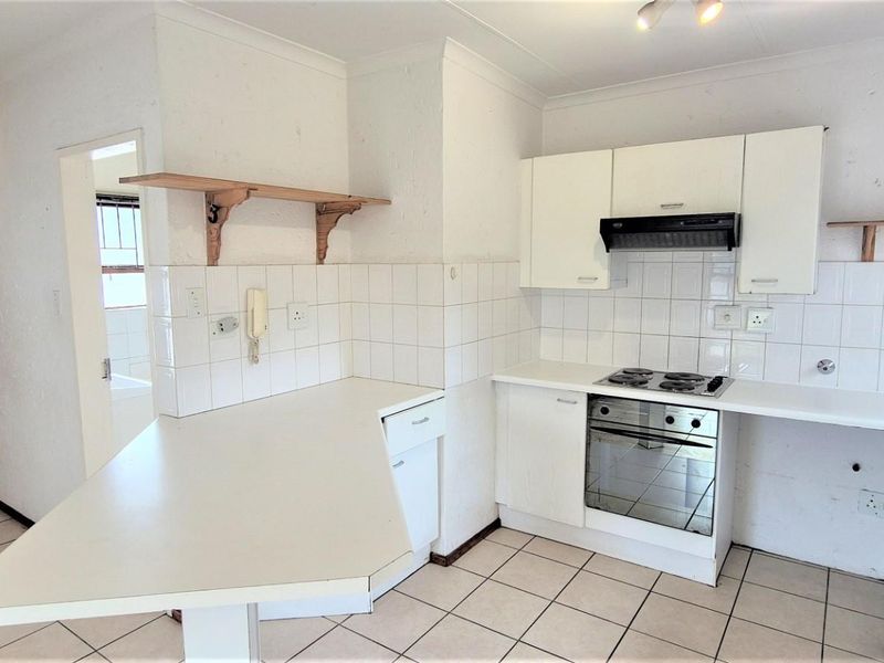 A functional kitchen featuring built-in cabinetry, an electric hob, oven, extractor fan, and a breakfast counter, finished with tiled flooring and a tiled backsplash.