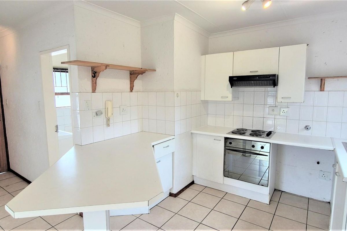A functional kitchen featuring built-in cabinetry, an electric hob, oven, extractor fan, and a breakfast counter, finished with tiled flooring and a tiled backsplash.