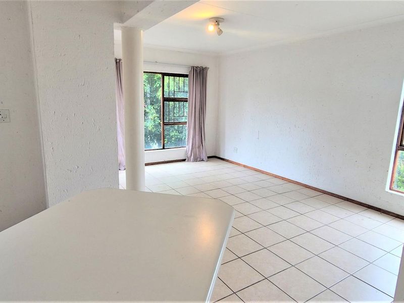 An open-plan living and kitchen area featuring tiled flooring, a structural column, and multiple windows with security bars, offering a blank canvas for renovation.