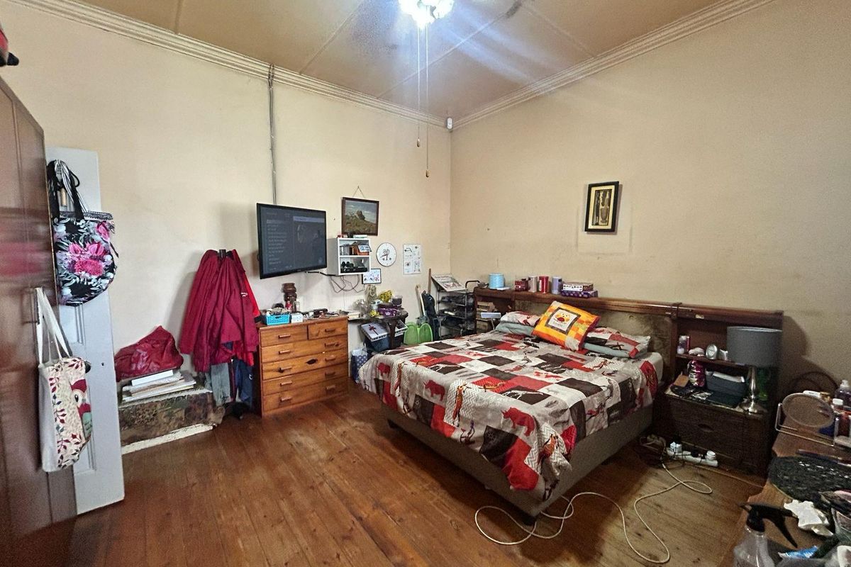 A spacious bedroom featuring original timber flooring, decorative ceiling cornicing, and a ceiling fan, offering a classic foundation for renovation.