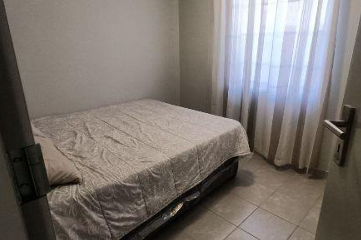 A compact bedroom featuring neutral tiled flooring and window treatments, offering a simple and functional living space.