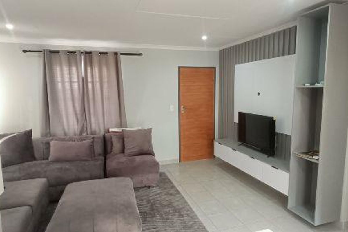 A well-maintained living room featuring tiled flooring, recessed downlights, and a modern built-in media unit with integrated shelving.