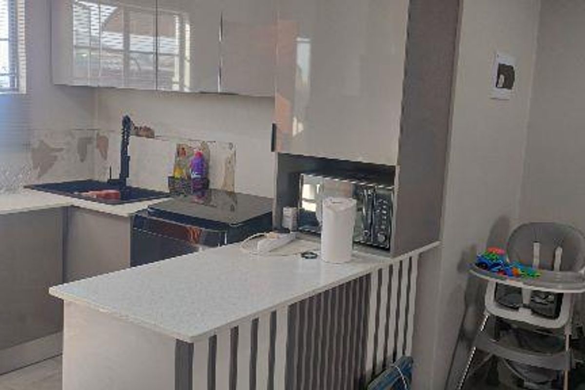 A compact kitchen featuring modern high-gloss cabinetry, stone countertops, a breakfast bar, and a built-in microwave, with some visible wall finish damage.