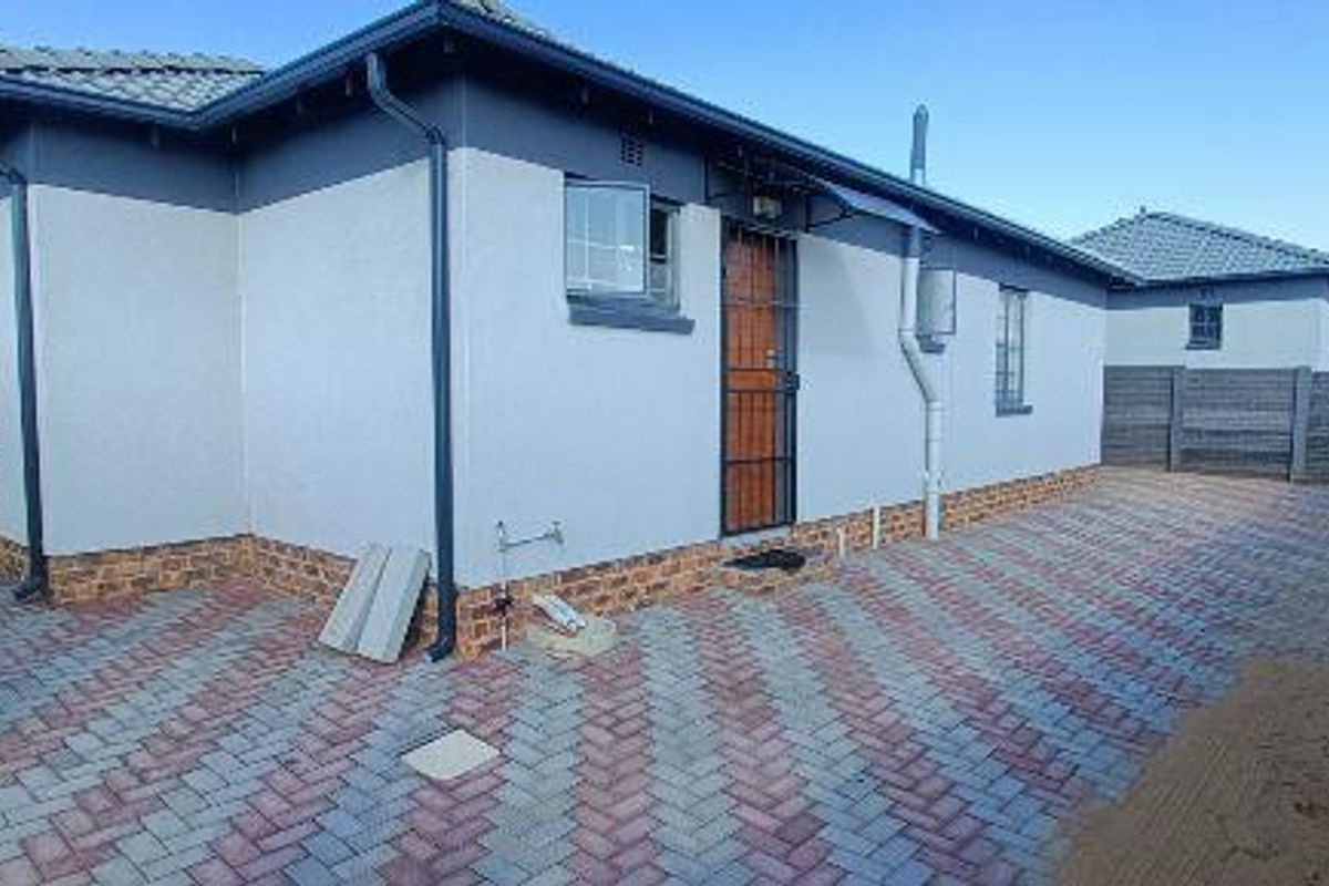 A well-maintained rear exterior view featuring a paved courtyard, secure entrance gate, and perimeter fencing.