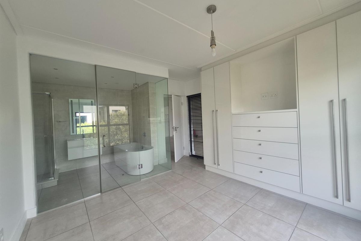 A modern bedroom featuring large format floor tiles, extensive built-in cabinetry, and an integrated glass-enclosed en-suite bathroom with a soaking tub and shower.