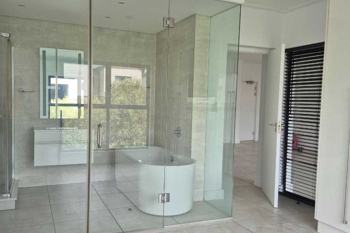 Modern bathroom featuring a glass-enclosed freestanding bathtub, wall-mounted vanity, and large format floor tiles in a bright, contemporary space.