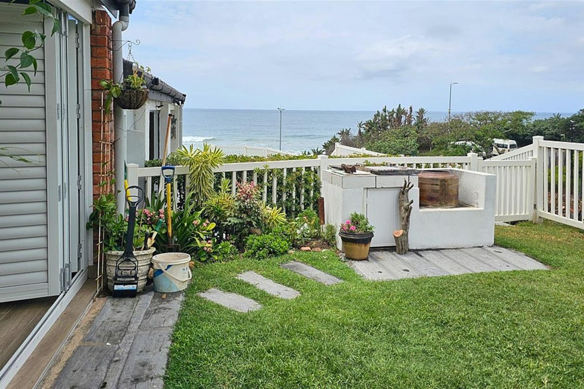 A private rear garden featuring a built-in braai area, lawn, and white picket fencing with direct ocean views.