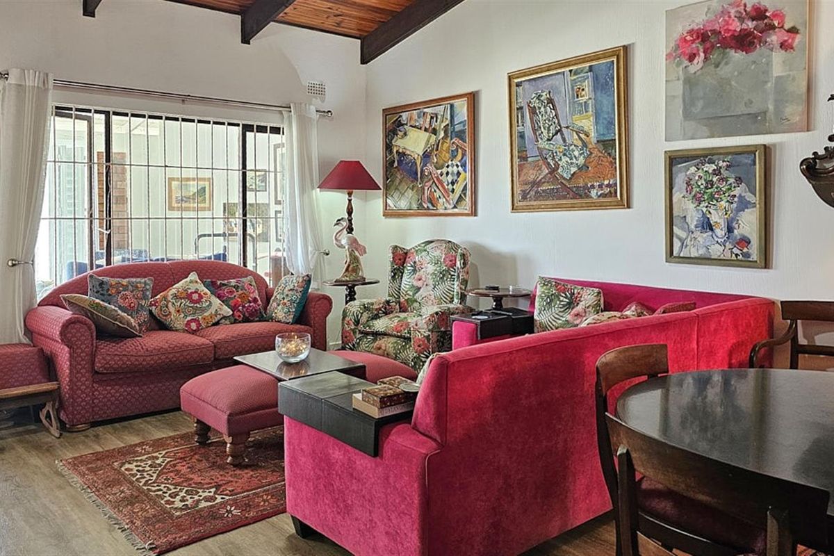 A cozy living room featuring exposed timber ceiling beams, laminate flooring, and large sliding glass doors with security bars leading to the exterior.