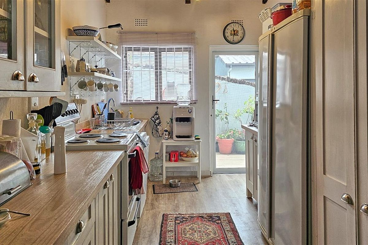 A functional galley-style kitchen featuring wood-look countertops, built-in cabinetry, a freestanding stove, and direct access to an outdoor patio area.