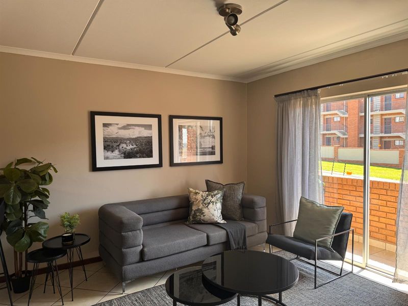 A well-lit living room featuring tiled flooring, modern track lighting, and a large sliding glass door providing access to an outdoor patio area.
