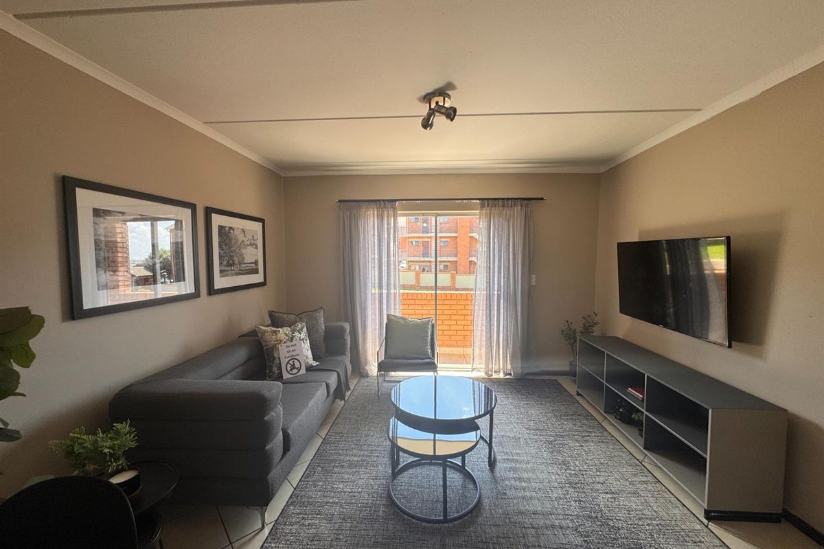 A well-maintained living room featuring tiled flooring, a coved ceiling, and a sliding glass door providing access to a balcony.