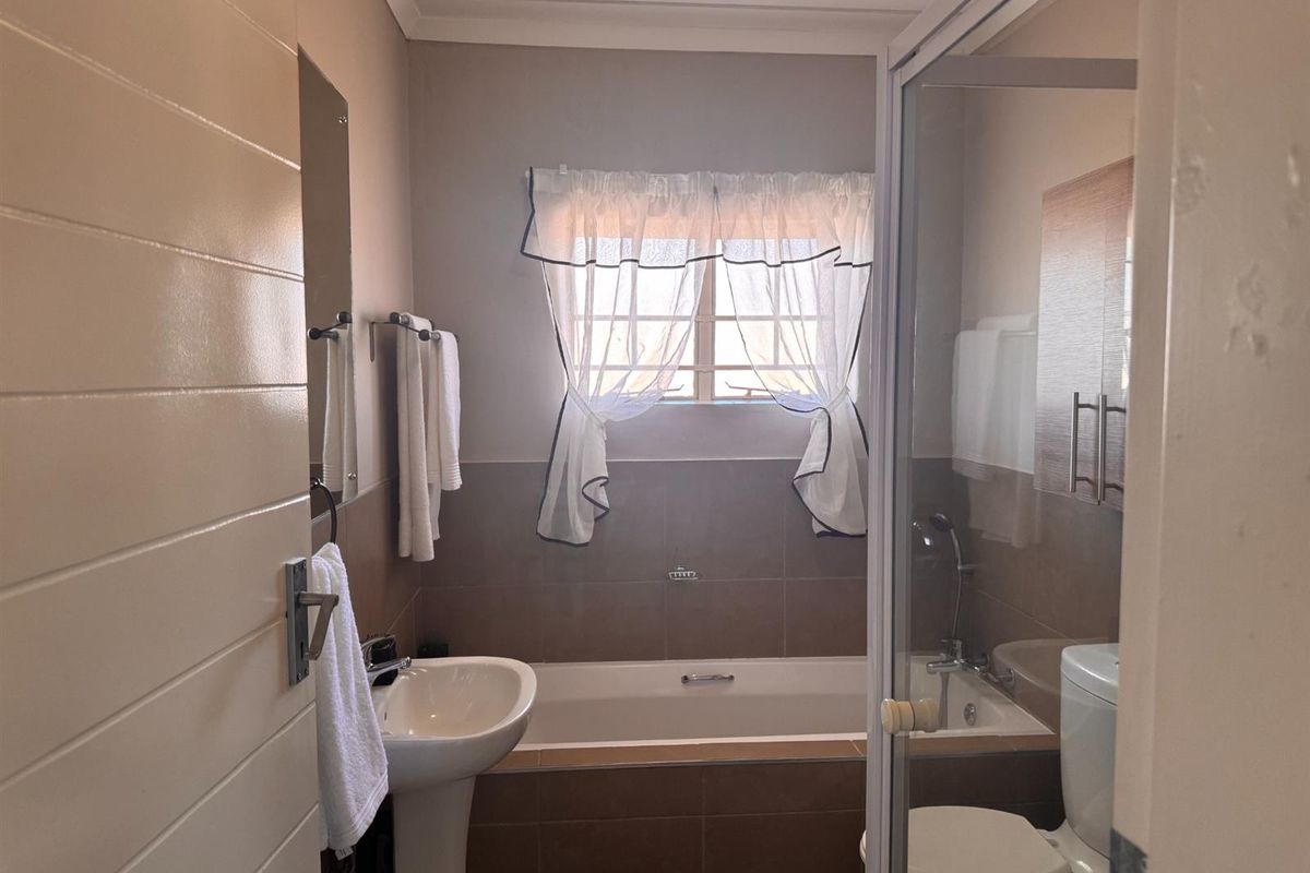A functional bathroom featuring a pedestal basin, built-in bathtub, separate shower enclosure, and toilet with neutral wall tiling.