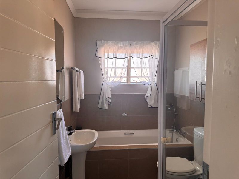 A functional bathroom featuring a pedestal basin, built-in bathtub, separate shower enclosure, and toilet with neutral wall tiling.