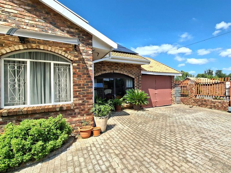 Front exterior view of a face-brick townhouse featuring a paved driveway, arched window detailing, and a secure garage entrance.