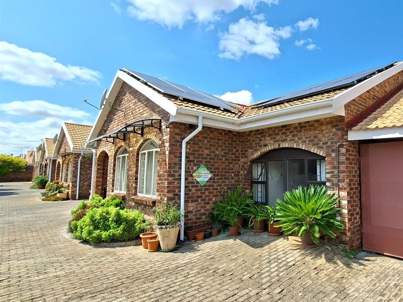 Exterior view of a brick townhouse featuring solar panels on the roof, arched window detailing, and a paved driveway area.