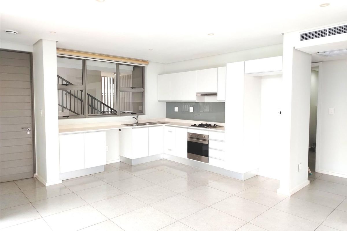 Modern open-plan kitchen featuring white cabinetry, integrated oven, gas hob, extractor fan, and tiled flooring in a bright, neutral space.