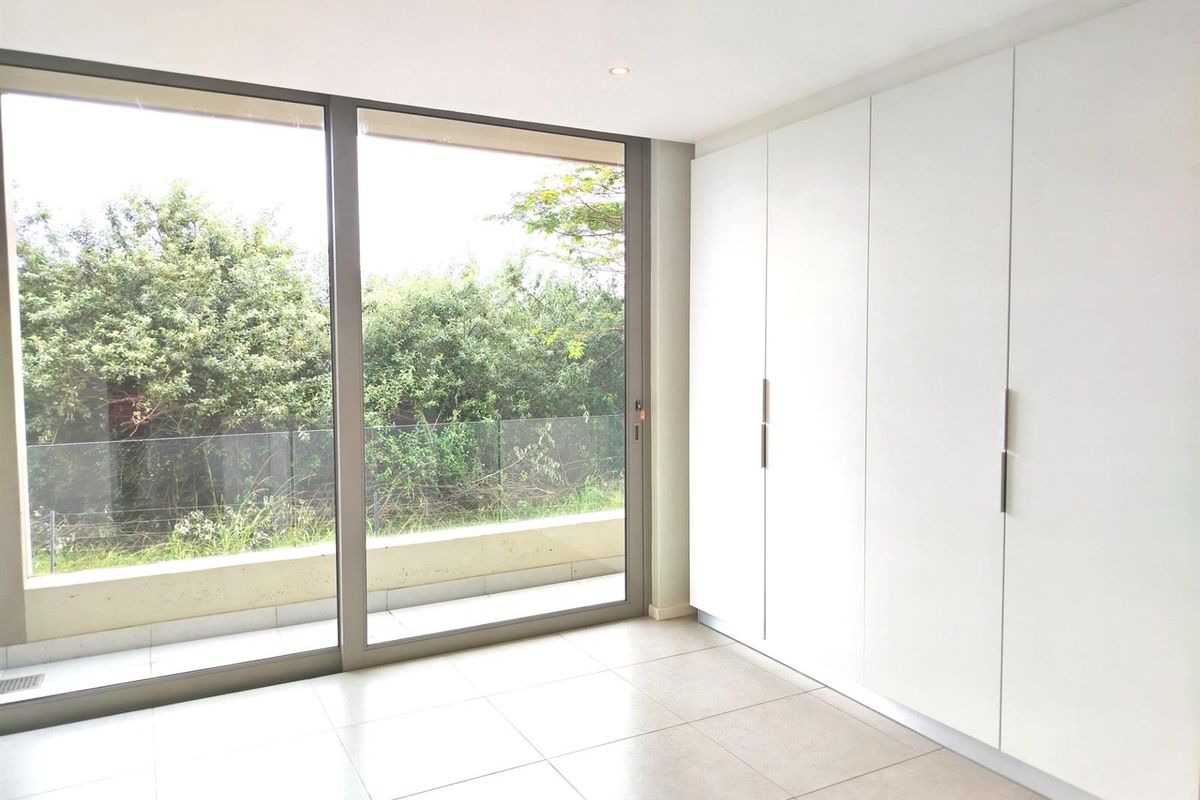 A bright bedroom featuring large floor-to-ceiling sliding glass doors, neutral tiled flooring, and extensive built-in floor-to-ceiling cabinetry.