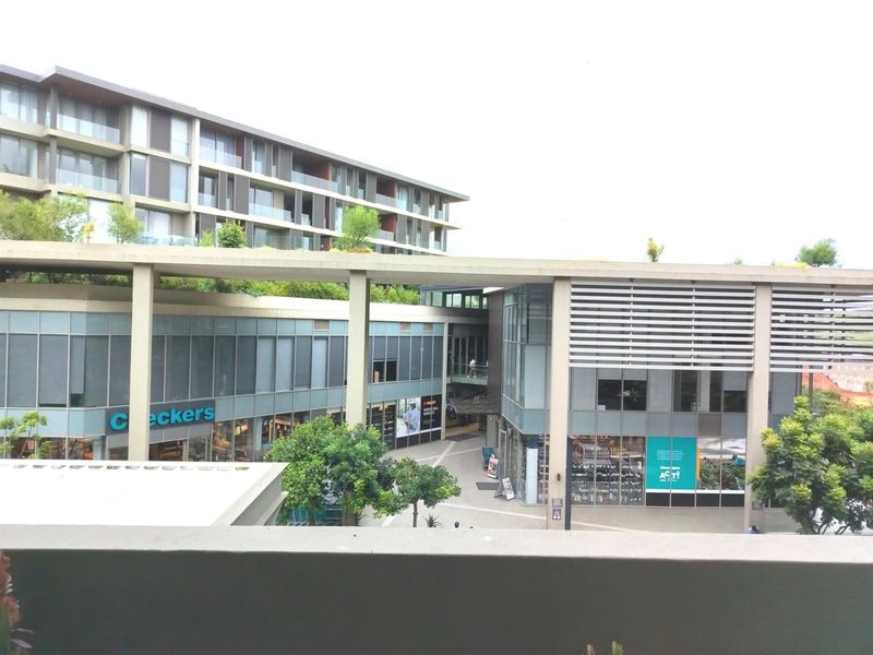 View of the modern apartment complex exterior and integrated retail space, showcasing contemporary architectural design and landscaped terrace areas.