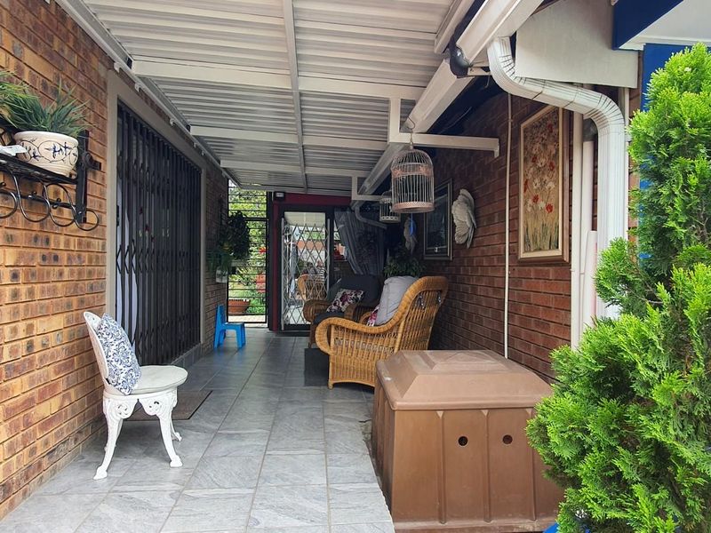 A covered patio area featuring face-brick walls, tiled flooring, and a corrugated metal roof structure, providing a sheltered outdoor living space.