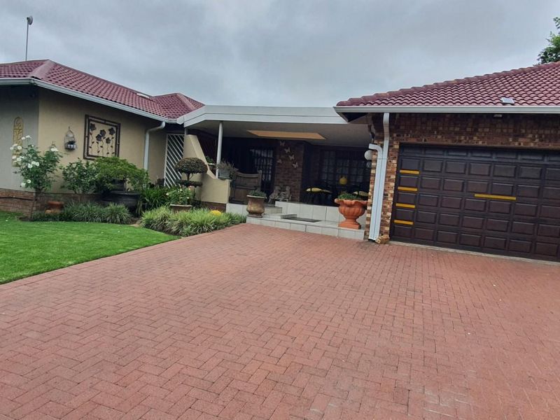 Front view of a single-story house featuring a paved driveway, double garage, tiled roof, and a covered entrance porch with landscaped garden.