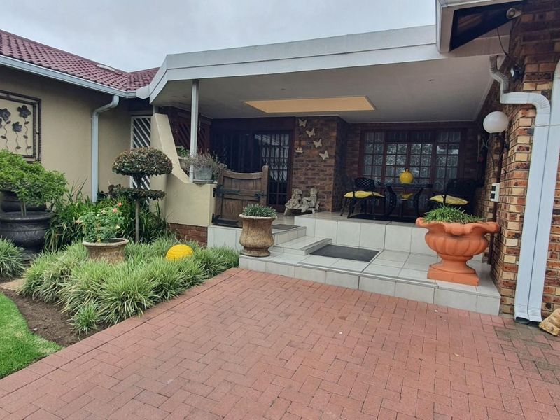 A covered patio area featuring tiled flooring, brick facade, and direct access to the garden and garage.