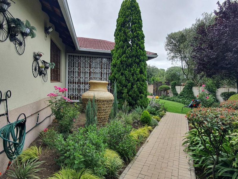 A well-maintained side garden featuring a paved walkway, established landscaping, and security gates on the building exterior.