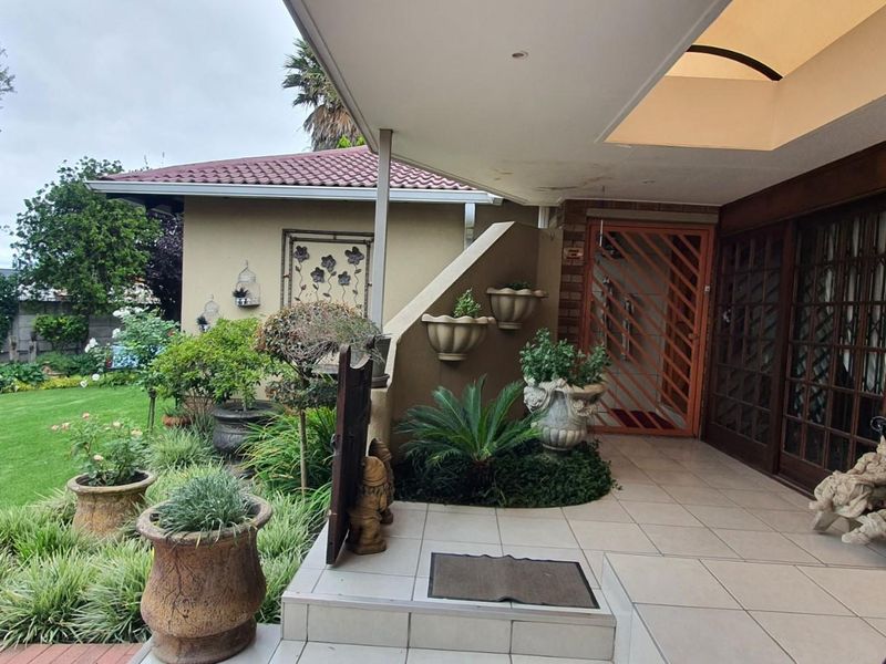 A covered patio area overlooking a well-maintained garden, featuring tiled flooring and direct access to the home through a security gate.