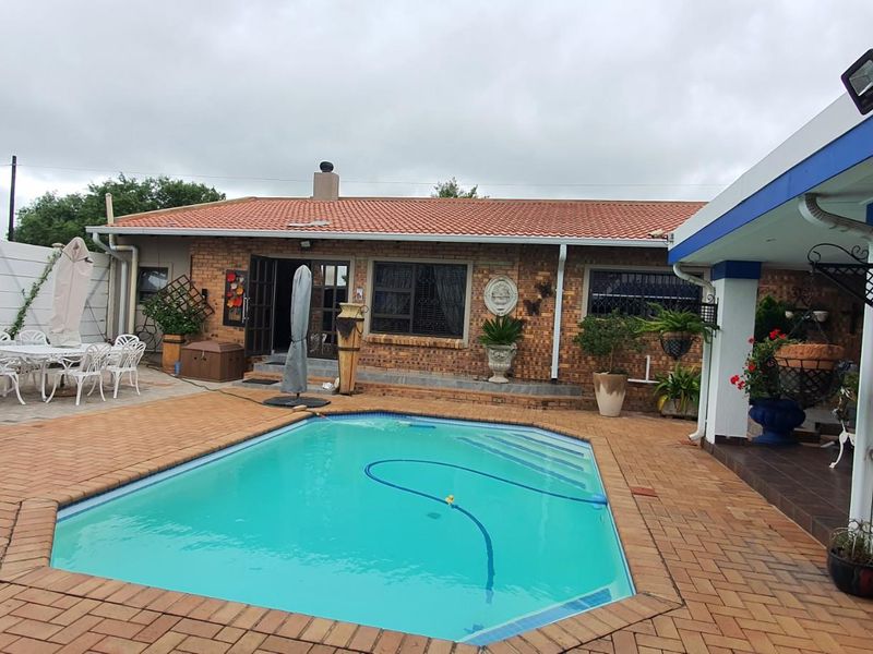 A spacious outdoor entertainment area featuring a swimming pool, brick-paved patio, and covered veranda, ideal for outdoor living and relaxation.