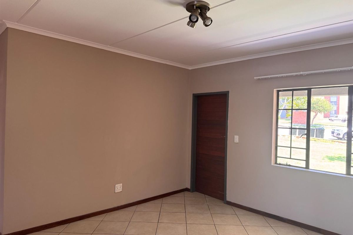 An empty living room featuring neutral wall paint, tiled flooring, a ceiling spotlight fixture, and a window with security bars.