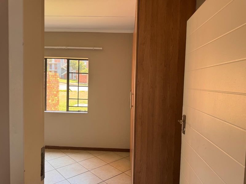 A bright, empty bedroom featuring tiled flooring and a built-in wooden wardrobe, offering a clean and neutral space ready for personalization.