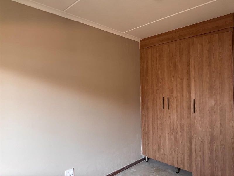 A clean, empty bedroom featuring neutral wall tones, tiled flooring, and a large, modern wood-finish built-in wardrobe.
