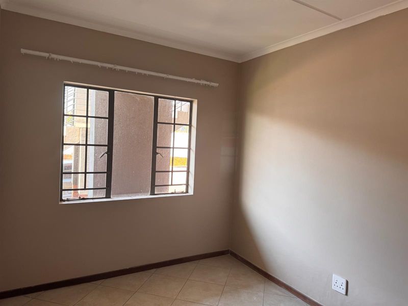 A clean, empty bedroom featuring neutral wall paint, tiled flooring, and a steel-framed window with an installed curtain rail.