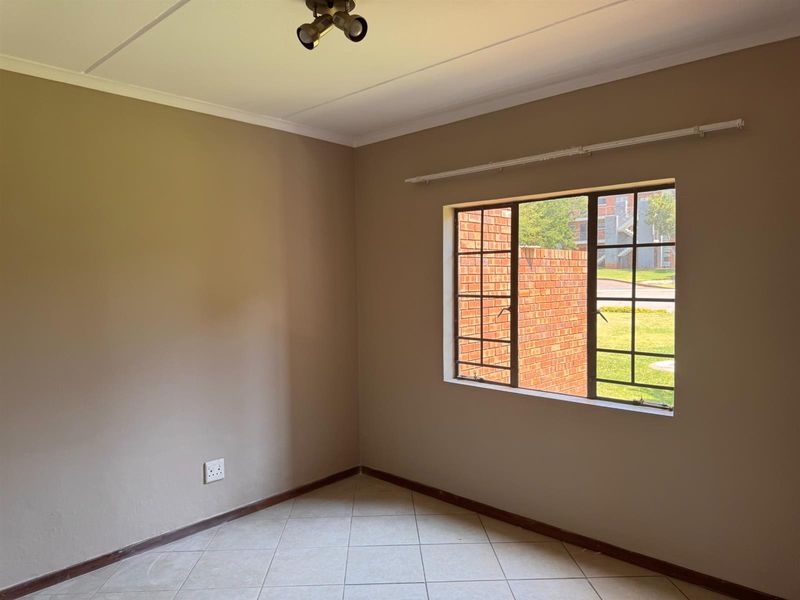An empty bedroom featuring neutral wall paint, tiled flooring, and a window with security bars, offering a blank canvas for personalization.