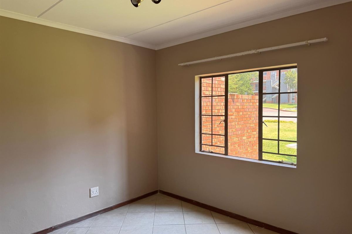 An empty bedroom featuring neutral wall paint, tiled flooring, and a window with security bars, offering a blank canvas for personalization.
